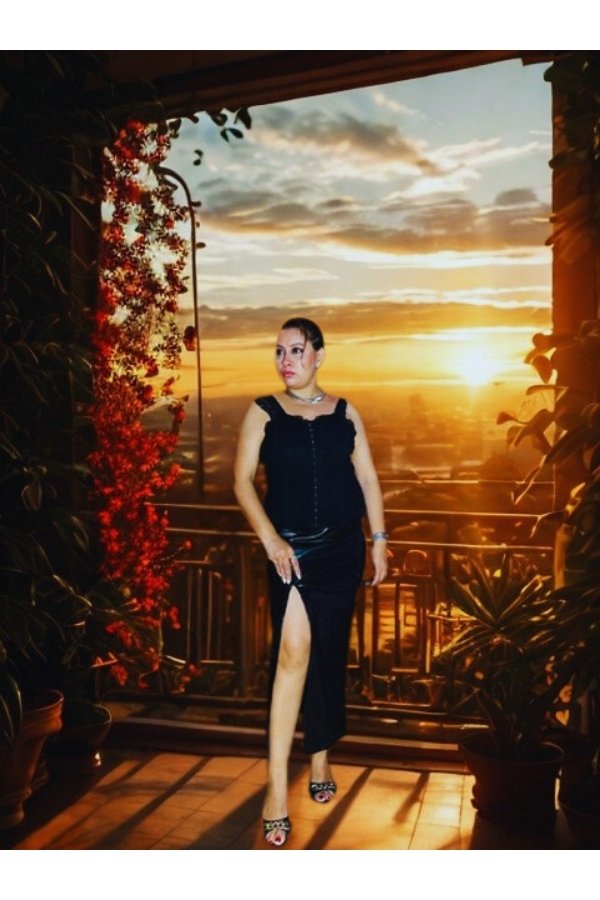 Curvy woman wearing a black corset slit dress on a balcony at sunset, perfect for elegant evening wear.
