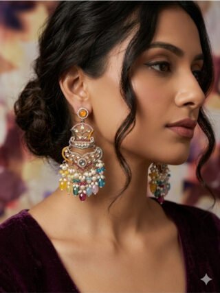 Model showcasing Melegant by LC multi-color pastel chandelier earrings featuring Kundan stones, seed pearls, and vibrant dangling gemstone drops against a dark purple velvet outfit