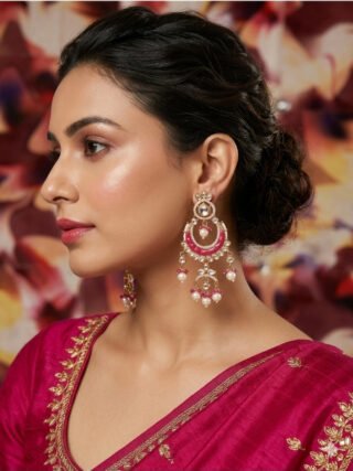 Close-up of a woman wearing traditional fuchsia pink Chandbali earrings with Kundan stones and hanging pearls from Melegant by LC, paired with a magenta silk saree.